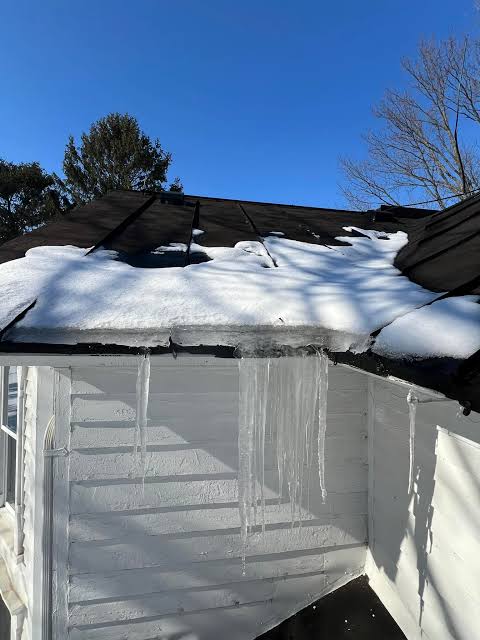 Heavy snow and ice dam buildup on a residential roof with long icicles hanging from the eaves.