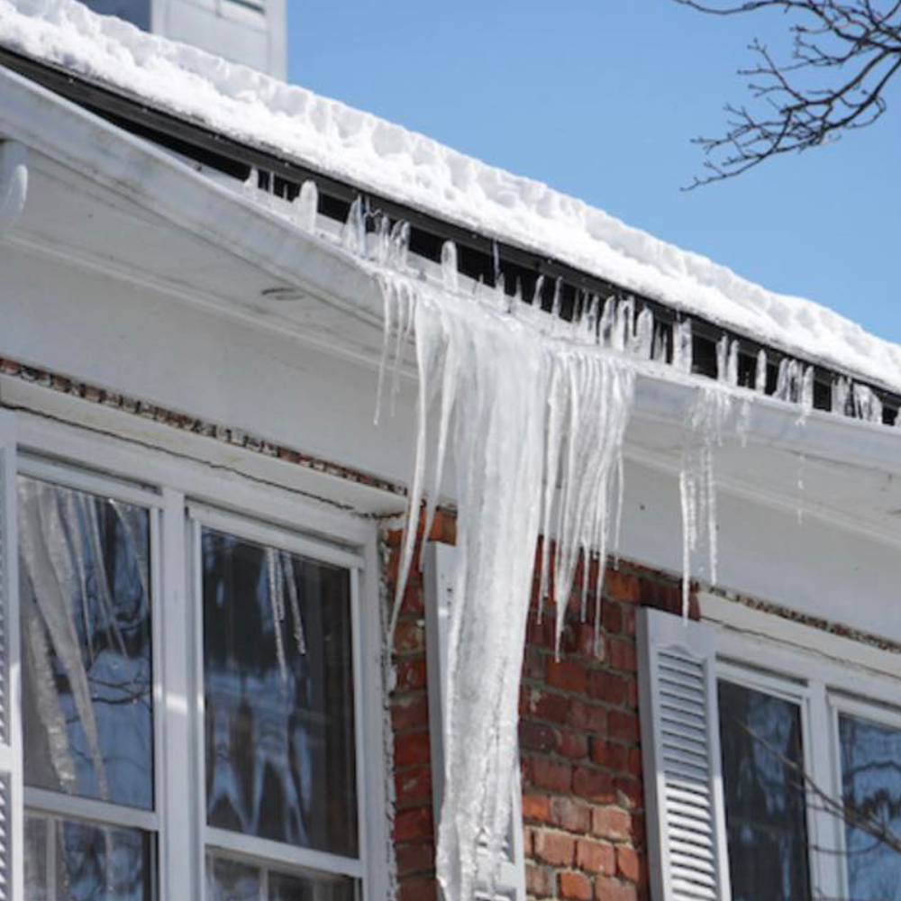 Large icicles hanging from snow-covered gutters and roof eaves on a home during winter.