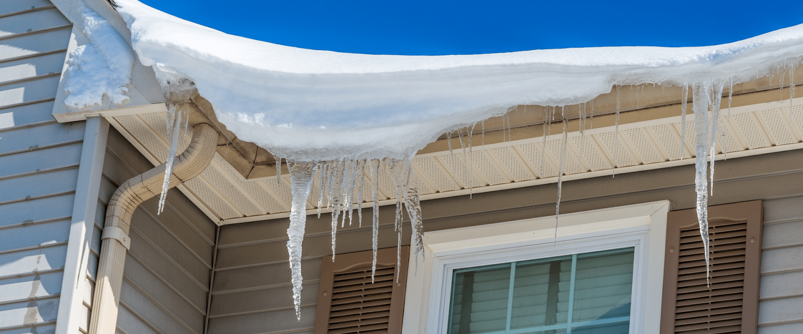 Ice buildup and icicles along a snow-covered roof edge caused by winter heat loss and poor attic ventilation