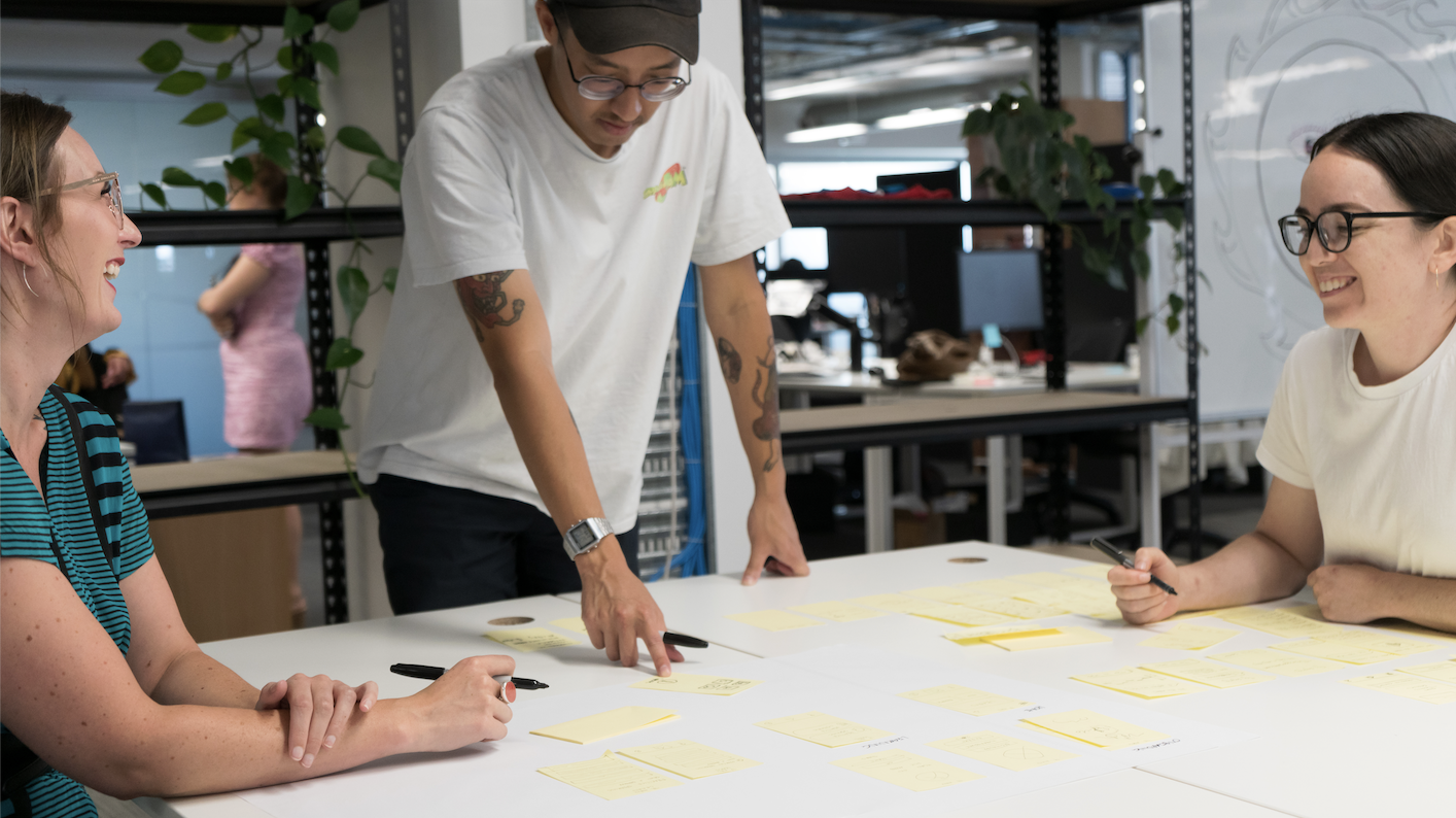 Three smiling people writing ideas on post it notes