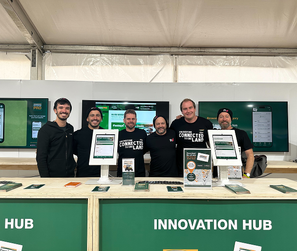 Six people standing behind an 'Innovation Hub' booth at a trade show or conference, wearing matching black t-shirts with 'Connected Lab' branding, displaying tablets and promotional materials on a green-branded table setup