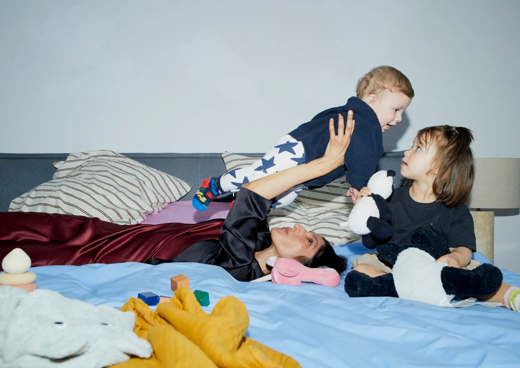 Mother on a bed holding up her baby with a toddler sitting close by