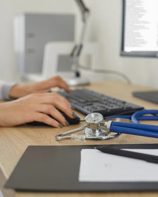 Hands typing on a computer with a stethoscope nearby