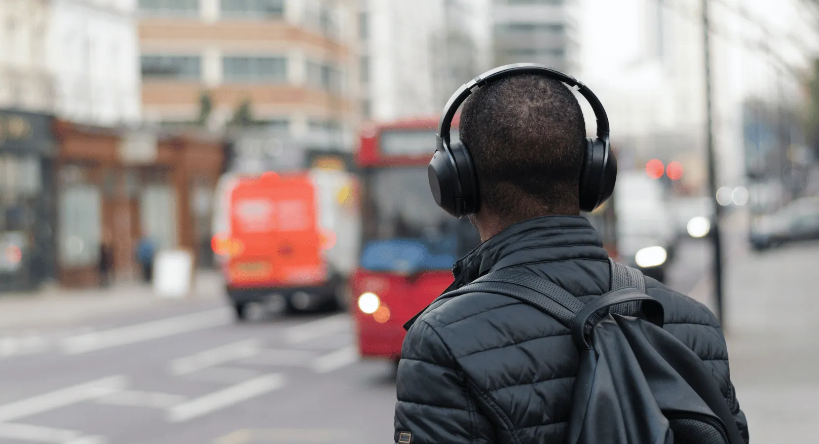 A man wearing headphones and a backpack standing on the street