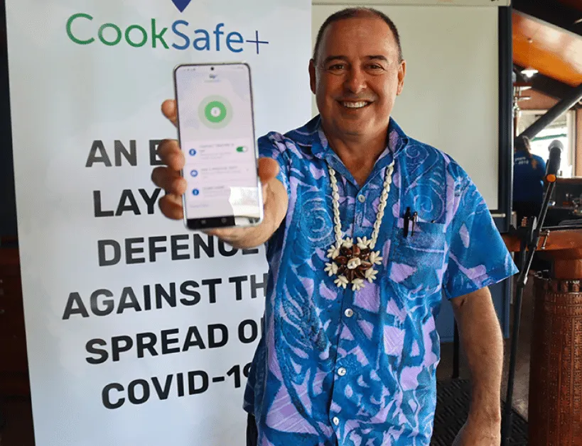Image of the Cook Islands PM holding a phone with the CookSafe Plus app