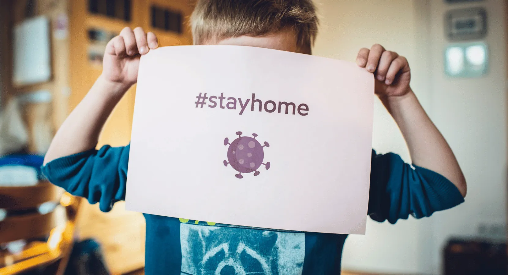 Child holding a piece of paper which says #stayhome and has a covid germ illustration