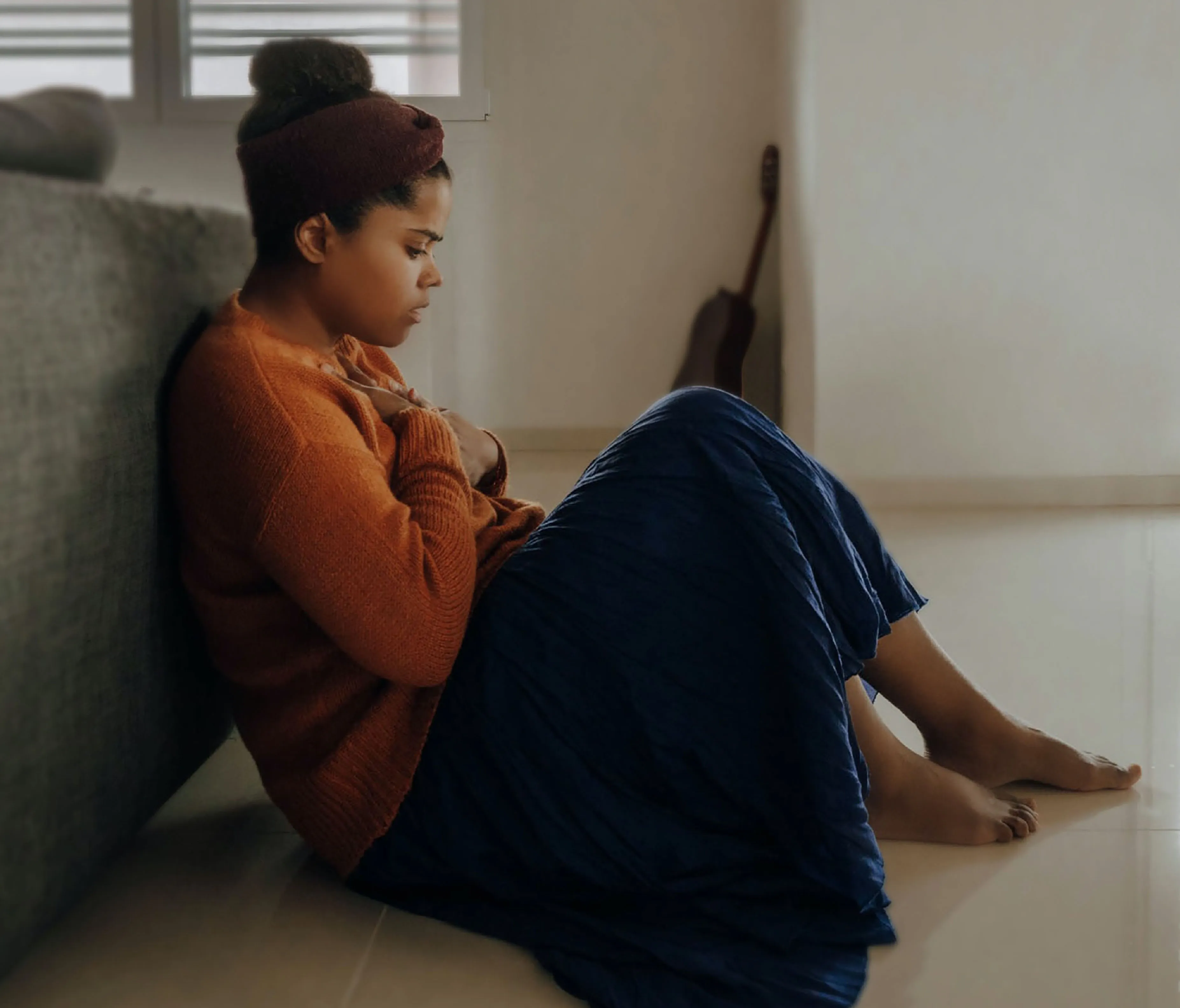 A woman sitting on the floor with her hands held to her chest