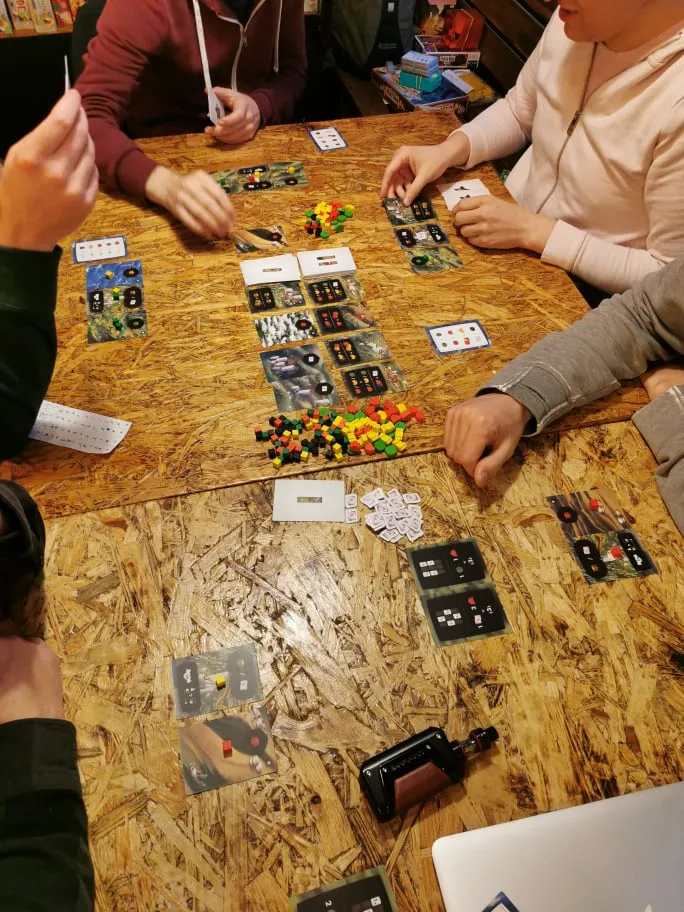A photo of a table inside of BBB cafe covered with card games. People playing.