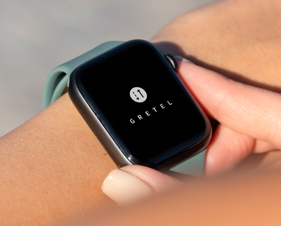A view looking down at an Apple Watch on a person’s wrist displaying the Gretel App logo