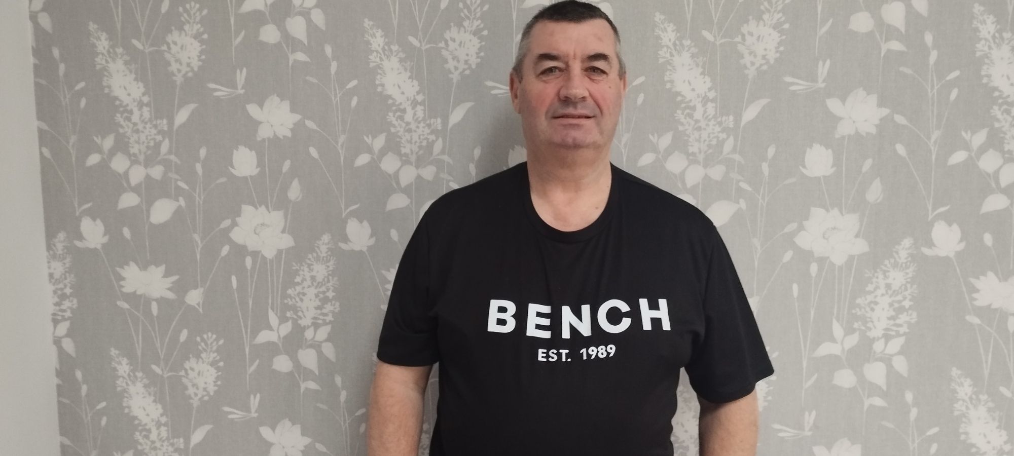 A man stands indoors, leaning against a wall.