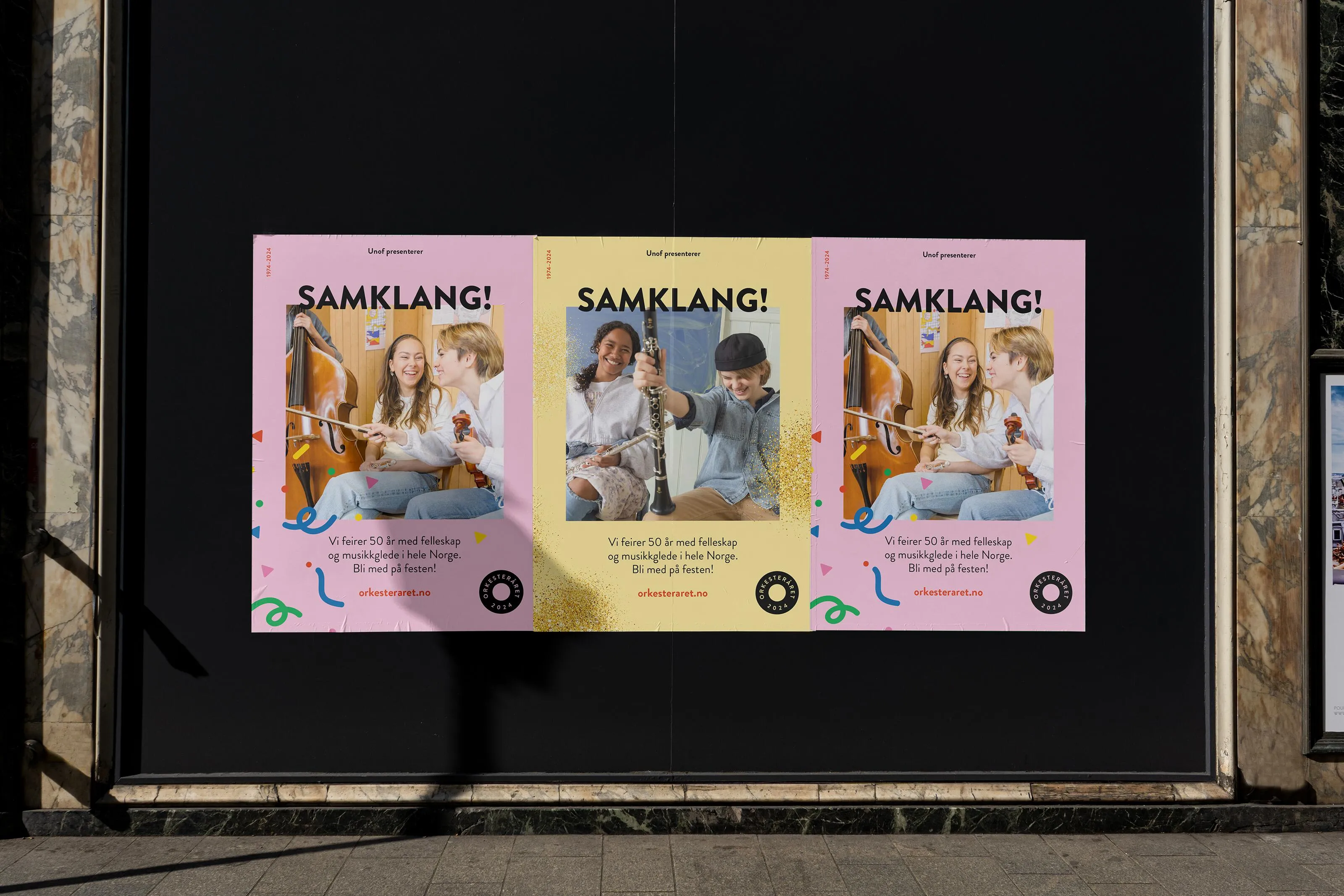 Three colourful "Samklang!" Orkesteråret 2024 posters on a dark wall, each showing joyful young musicians and confetti graphics promoting nationwide orchestra celebrations.