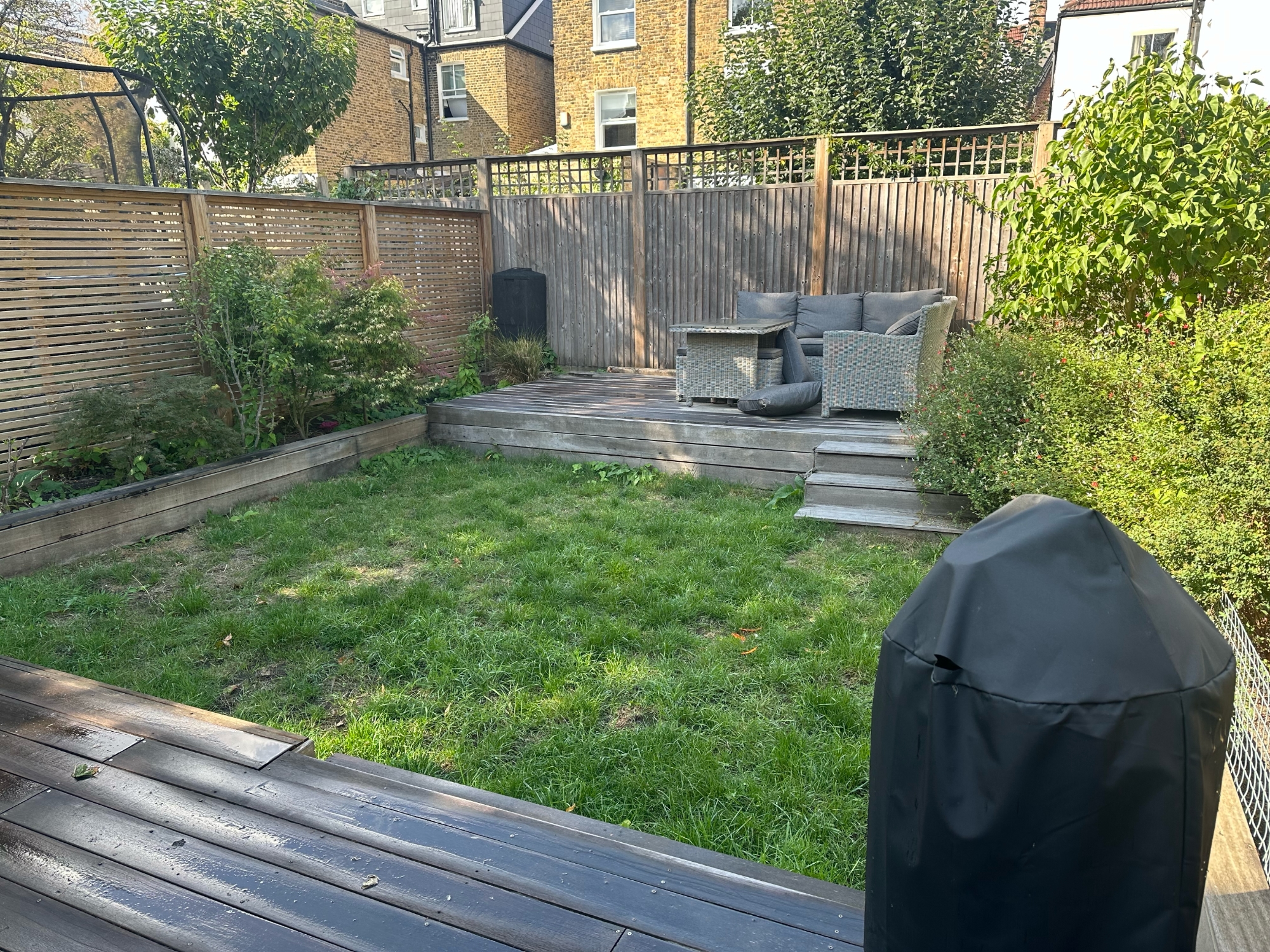 Before view of family garden showing existing timber deck, lawn, covered BBQ and established planting in raised sleeper beds