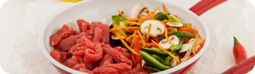 מחבת עם בשר חתוך גס וירקות טריים כמו גזר, פטריות, ופלפלים ירוקים.