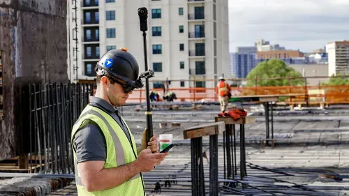 A construction worker using a 3D camera and his smartphone.