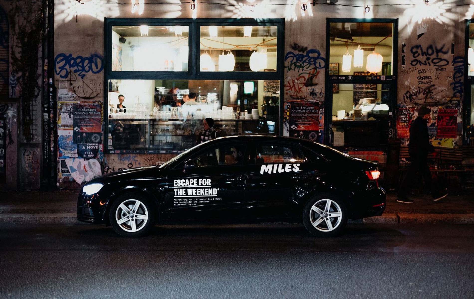 Miles car parked on the side of the road at night in front of restaurant, showcasing the brand identity design