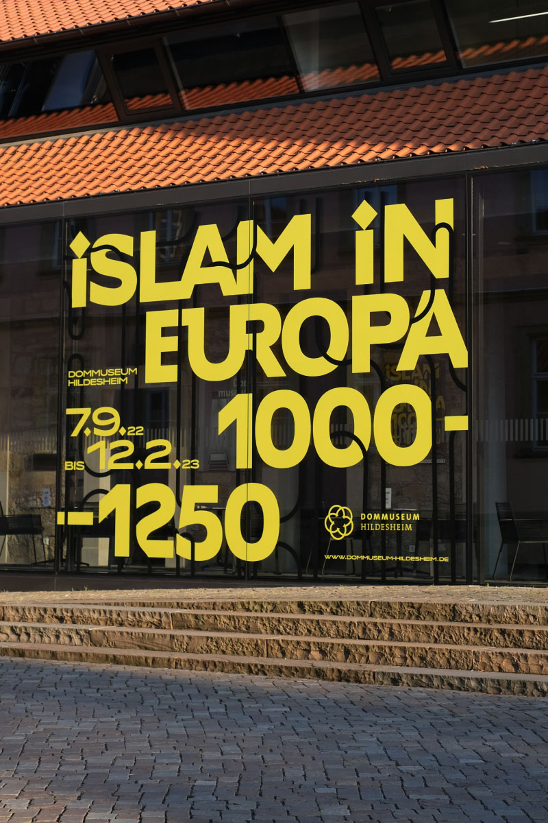 Exhibition Branding reading "Islam in Europa 1000-1250" in bold yellow on glass at Dommuseum Hildesheim.