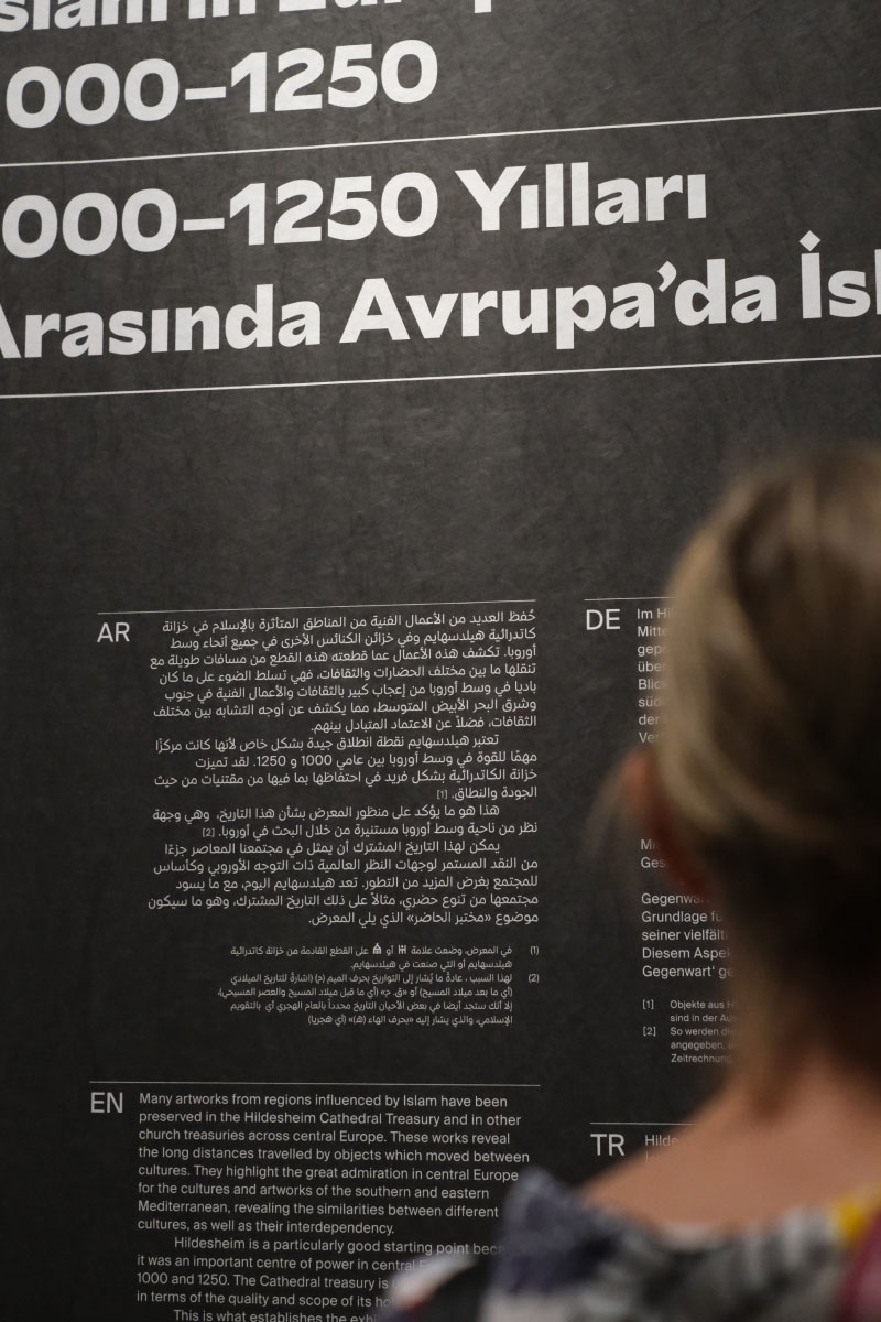 Person reading a black information board with white text in arabic, german, english and turkish, as part of the brand identity design