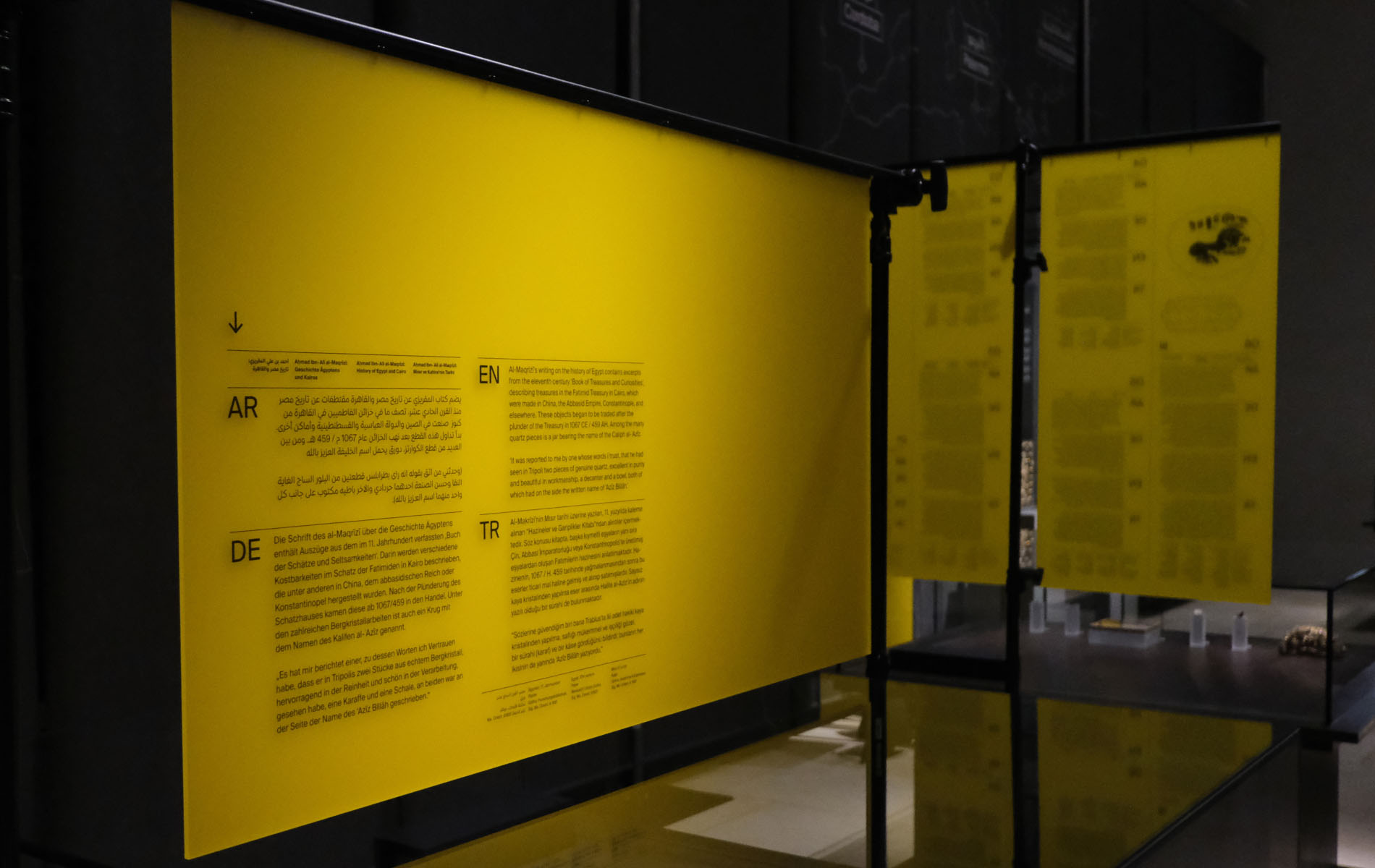 Photo of several yellow information boards in a museum containing black text in four different languages. In the background are several exhibits in a glass box, as part of the brand identity design