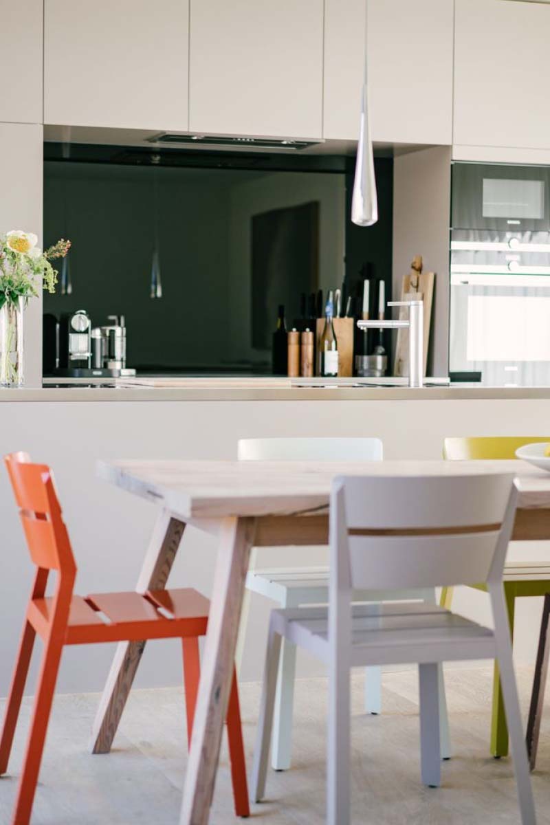 Interior of a modern black and white kitchen with colorfull chairs at a wooden table.