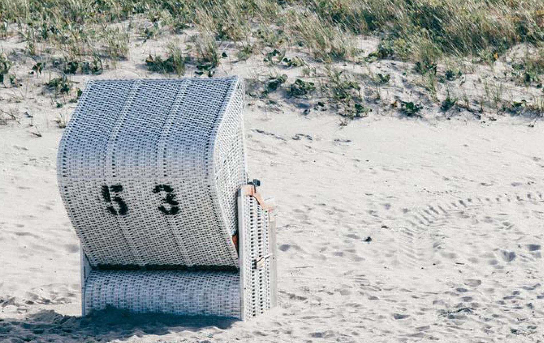 A beach chair with the number 53 on a sunny beach with some grass in the background.