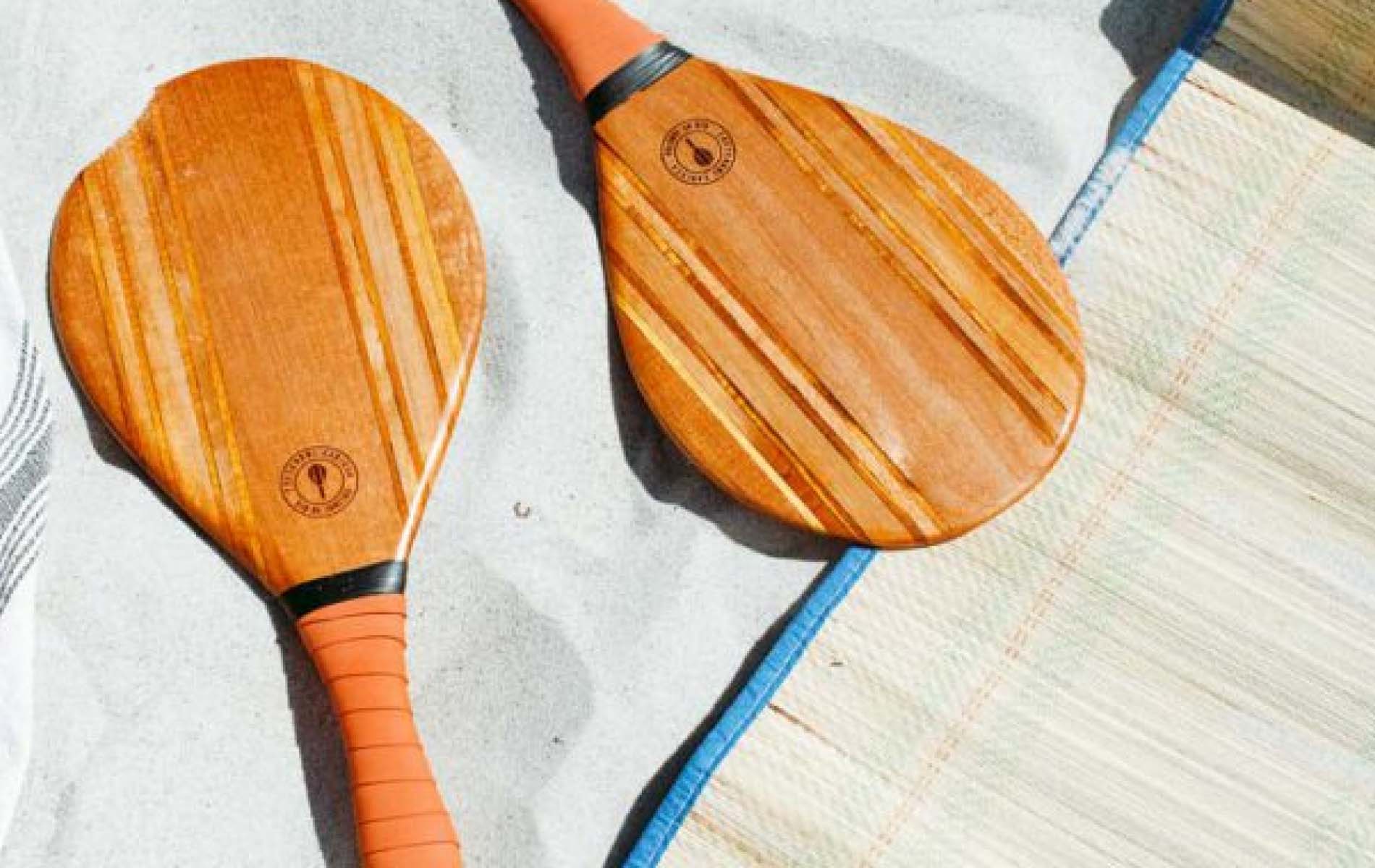 A beach bat set with orange grip-tape lying on sunny sand