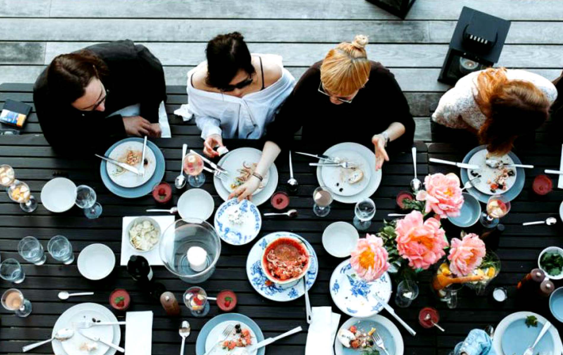 A bird's eye view photo of a black table with a set table of food and a large flower sit a group of people chatting for content creation