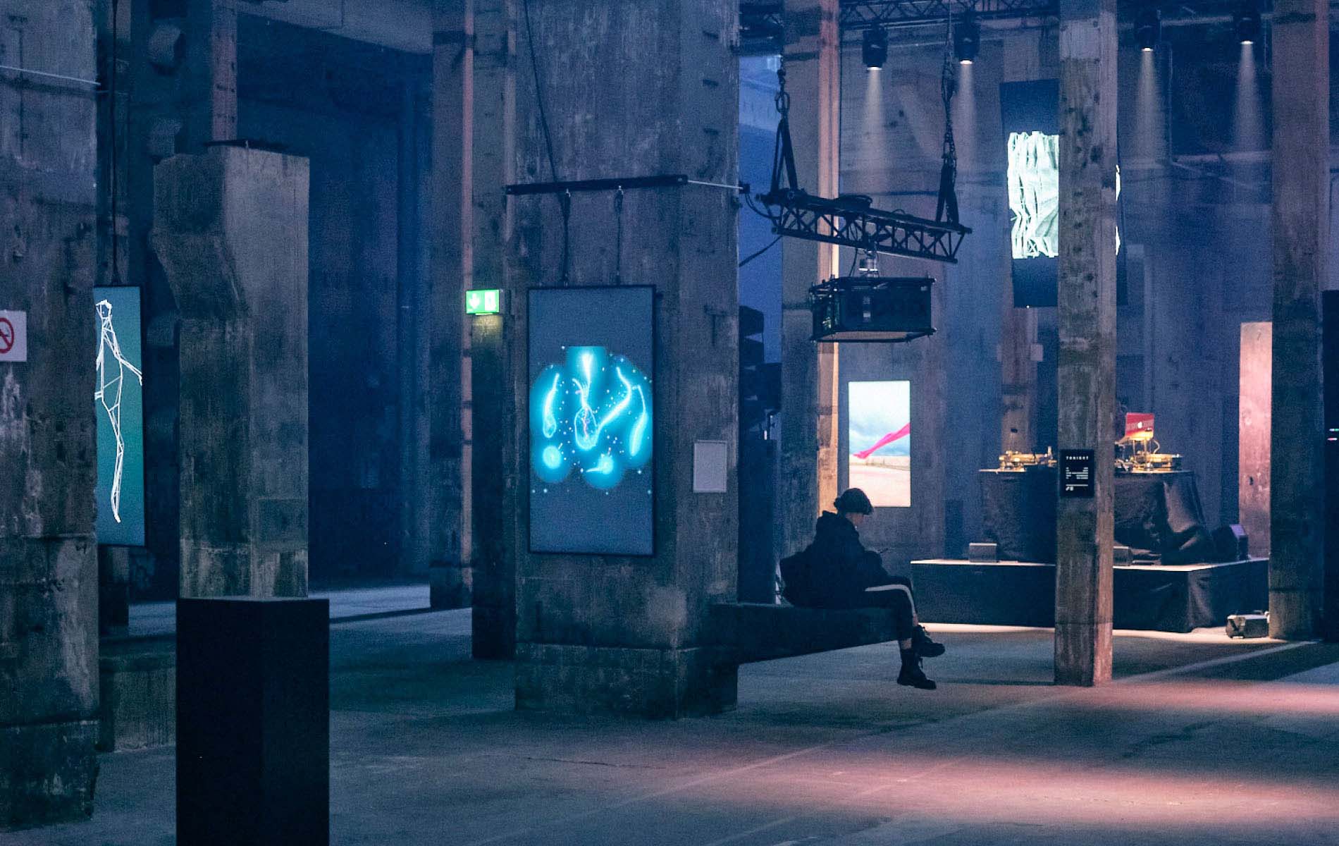 A dark room with high ceiling and art work made from screens hanging on the pillars of the room