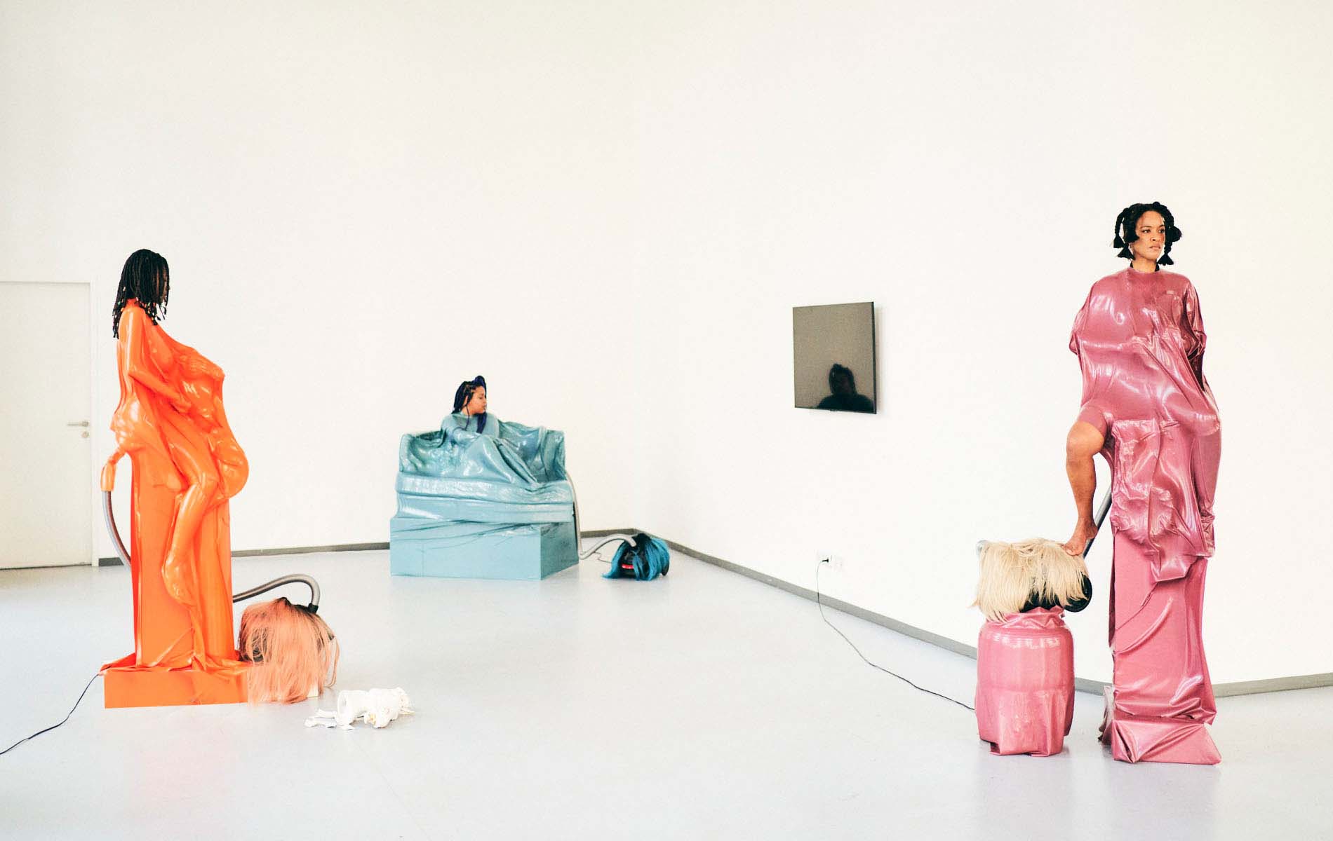 Art Installation cosisting of three person in it dressed in colorful material and standing in objects coverd in the same material, that are part of the installation