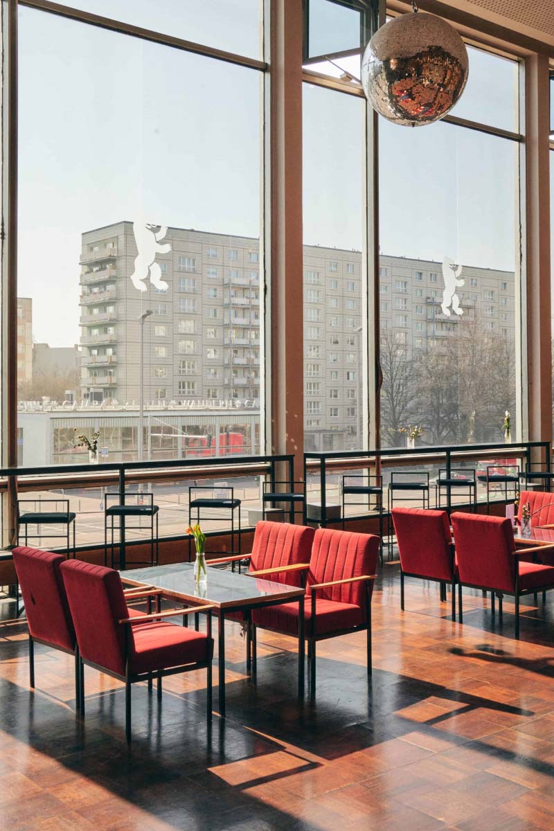 Bright room with big windows and a few tables and barstools next to the window and a disco ball is hanging from the ceiling