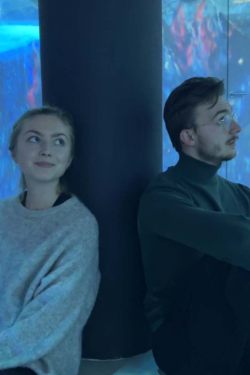 Two people sitting next to each other against a pillar looking at something