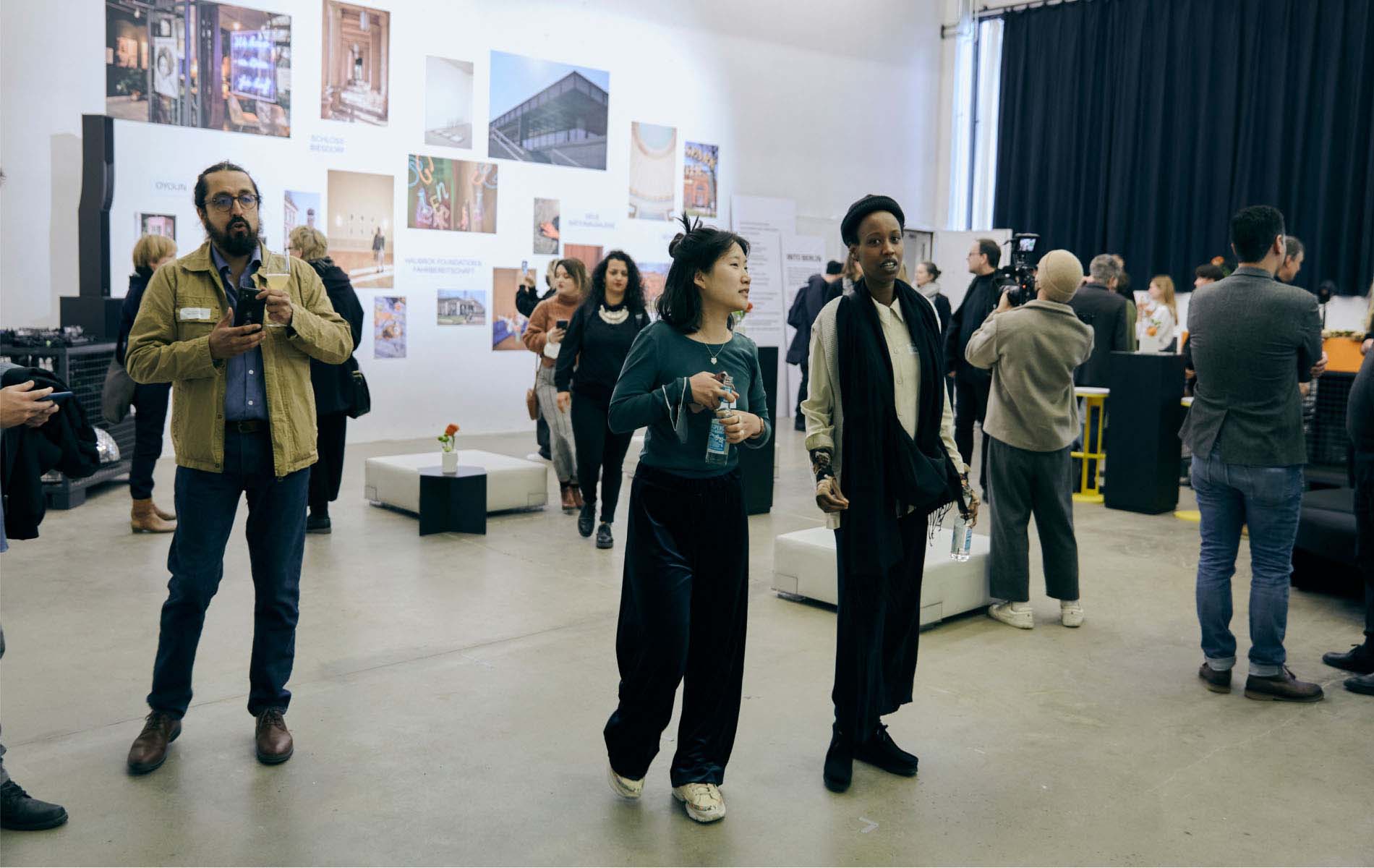 An exhibition room with a crow of people walking around, talking to each other while inspecting the pieces of work hanging there, as part of the content creation