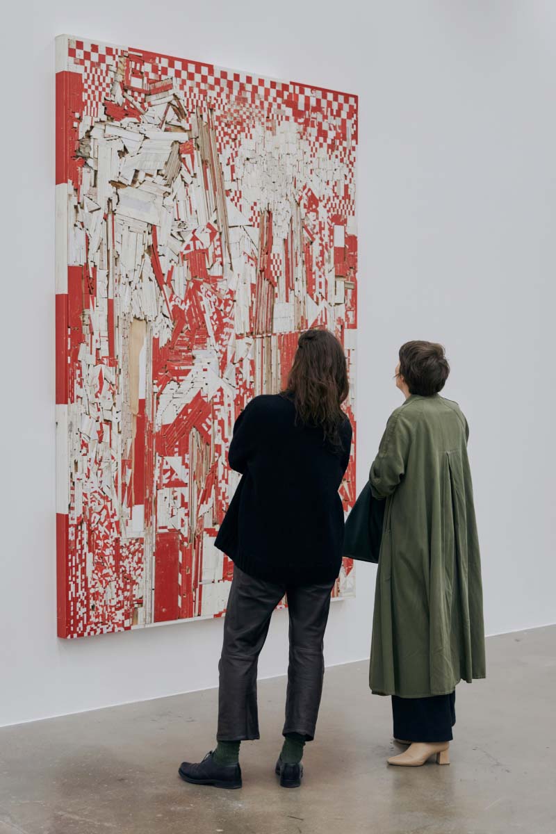 Two people standing in front of a big red colored artwork inspecting it and facing their backs to the camera