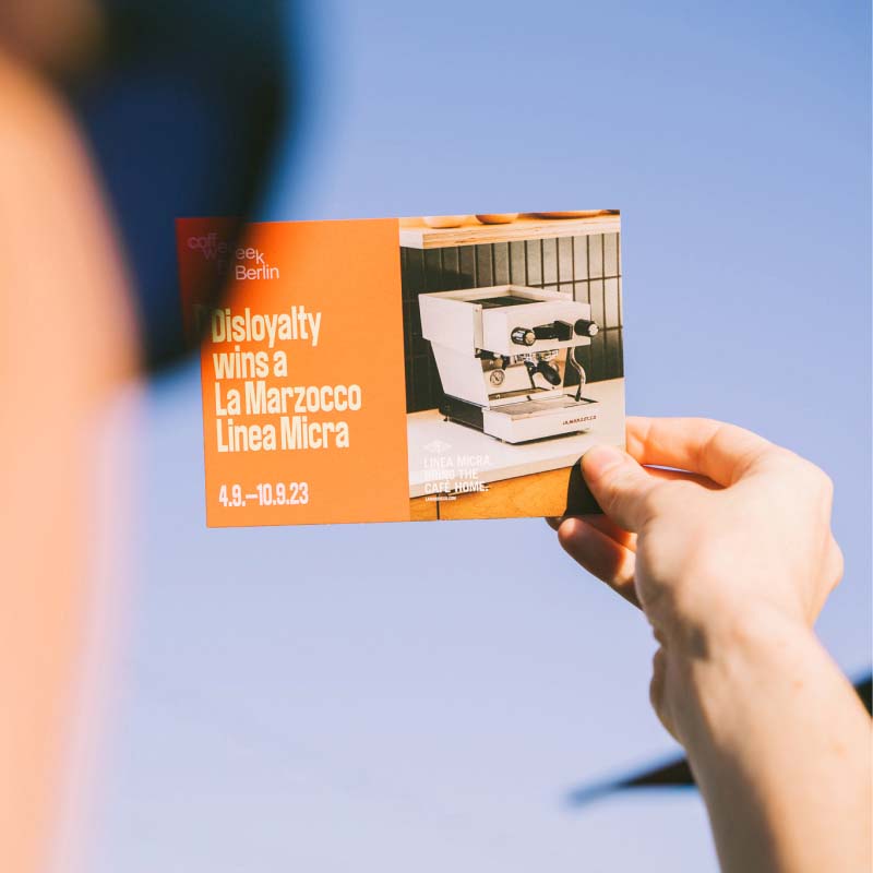 A person holding a a postcard-sized sheet of paper in their hand announcing the Coffee Week, as part of the communication design