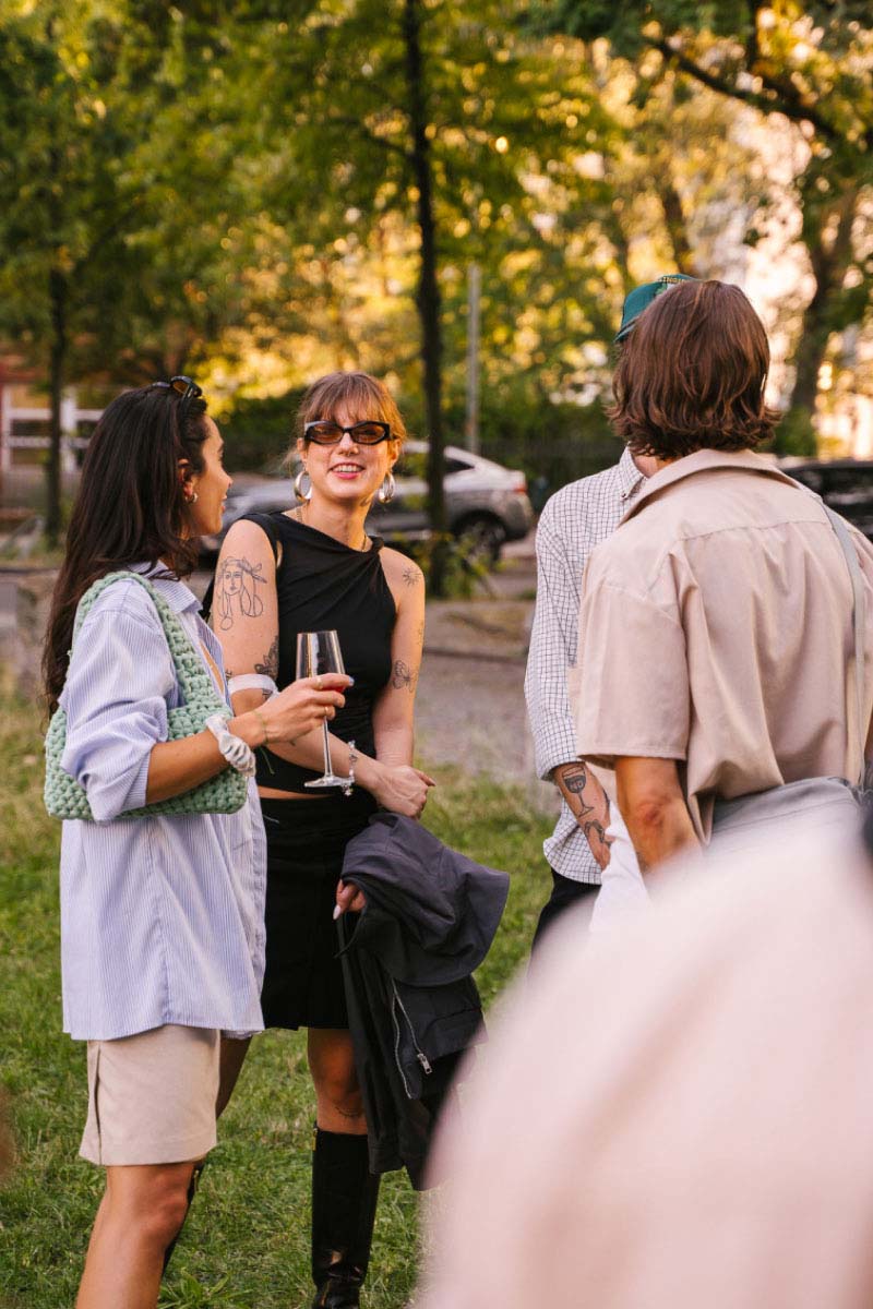 Four people standing in a small round talking and drinking a glass of wine