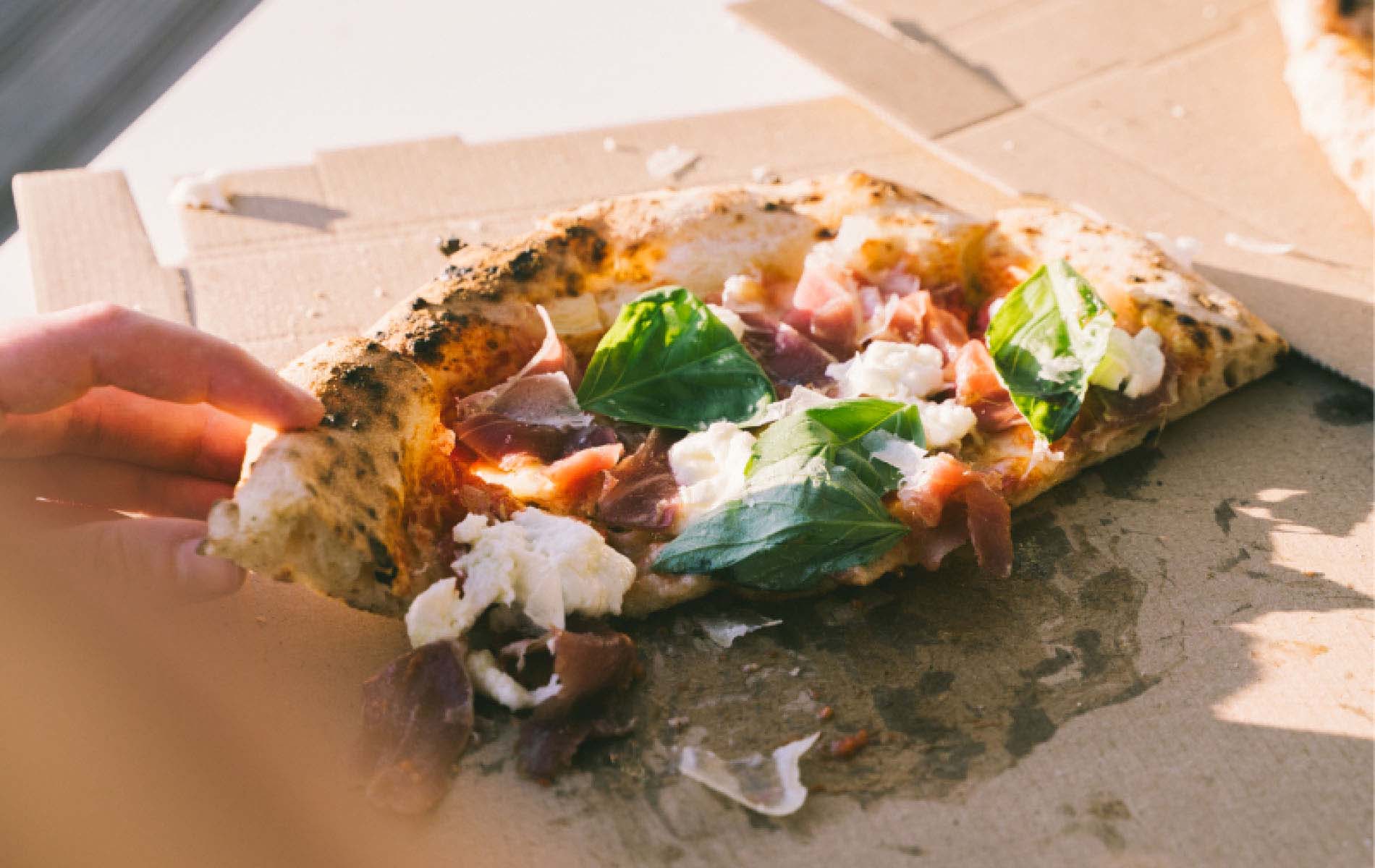 The half of a pizza with lots of cheese, ham and basil laying on a pizza box