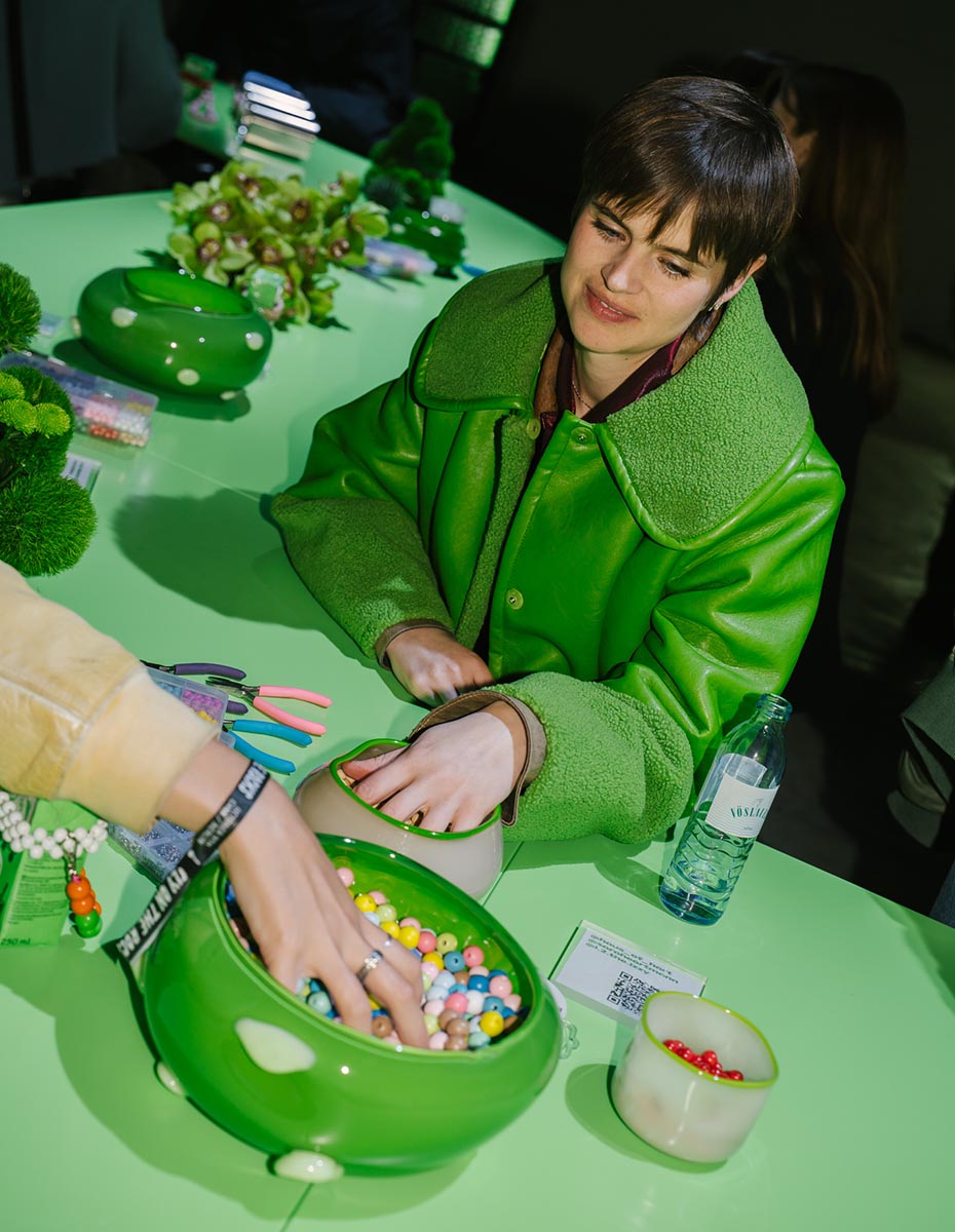 Guest selecting colorful beads at a bright green craft table during an Oatly event, captured by a creative agency/branding agency in Berlin.