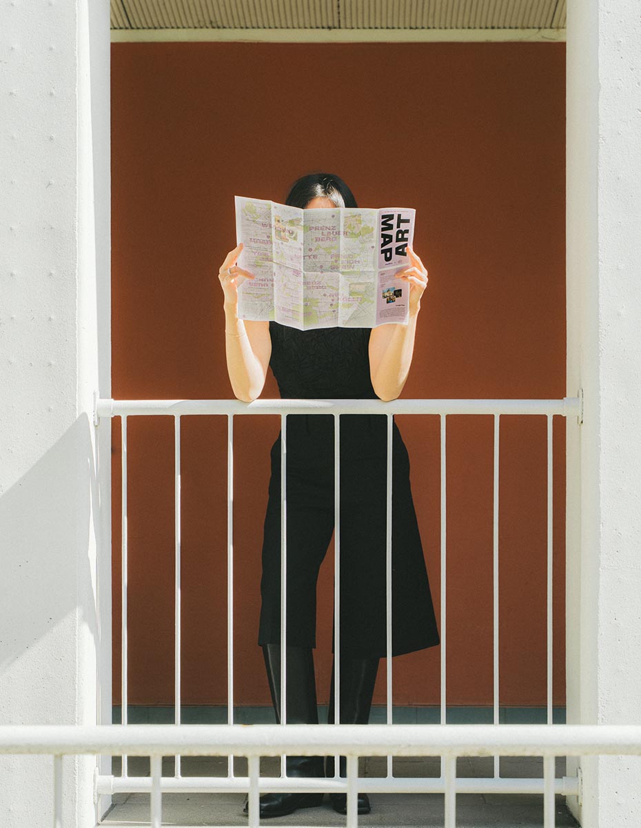 A woman reading an art map on a balcony, captured by a Creative Agency and Design Studio focusing on Corporate Design, UX Design, and Content Creation for brands