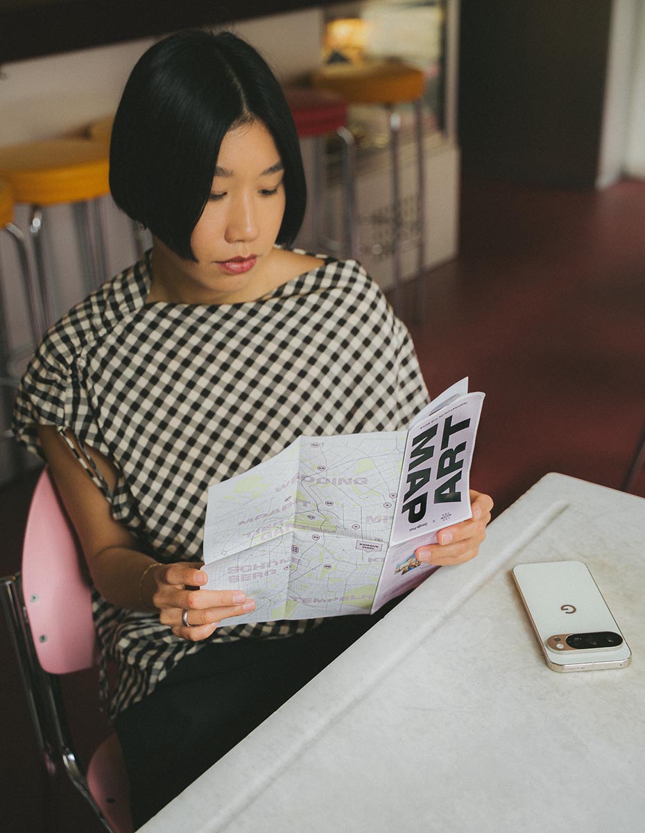 A woman reading an art map in a café with a Google Pixel phone beside her, created by a Full-Service Agentur offering Content Creation, Social Media Management, and Branding services.