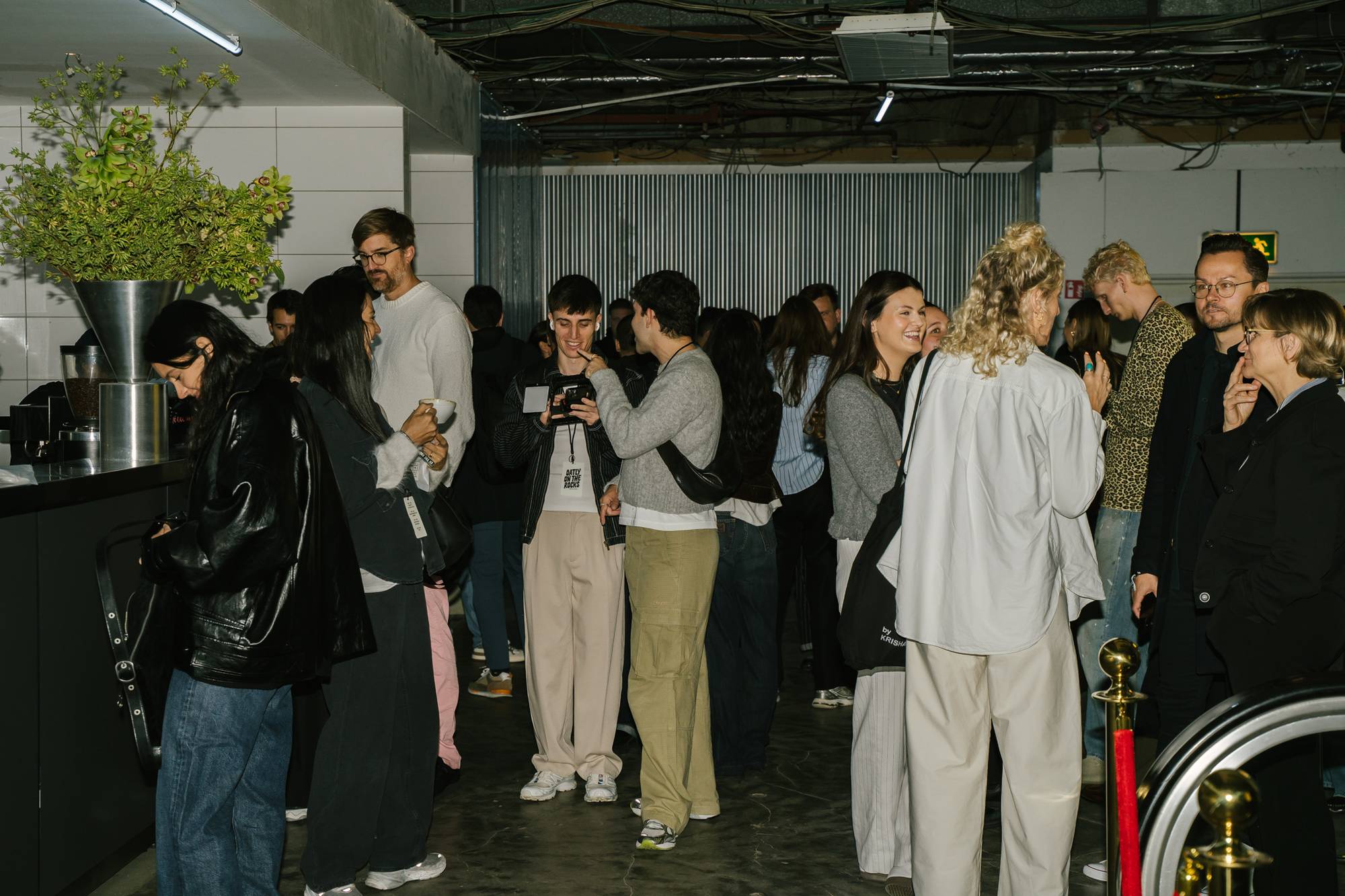 Guests gathered near the bar area at the Oatly Matcha launch event, chatting, taking photos, and queuing for drinks in a lively and modern industrial space.