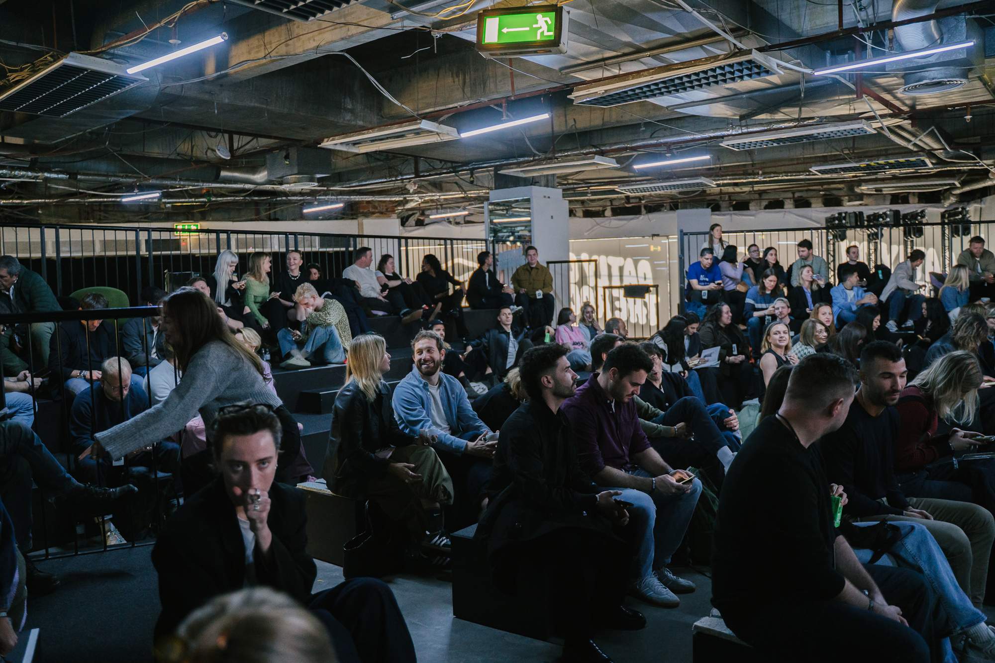 A wide crowd shot of the Oatly Matcha launch event showing attendees seated and mingling in an industrial-style venue with neon signage and ambient lighting.
