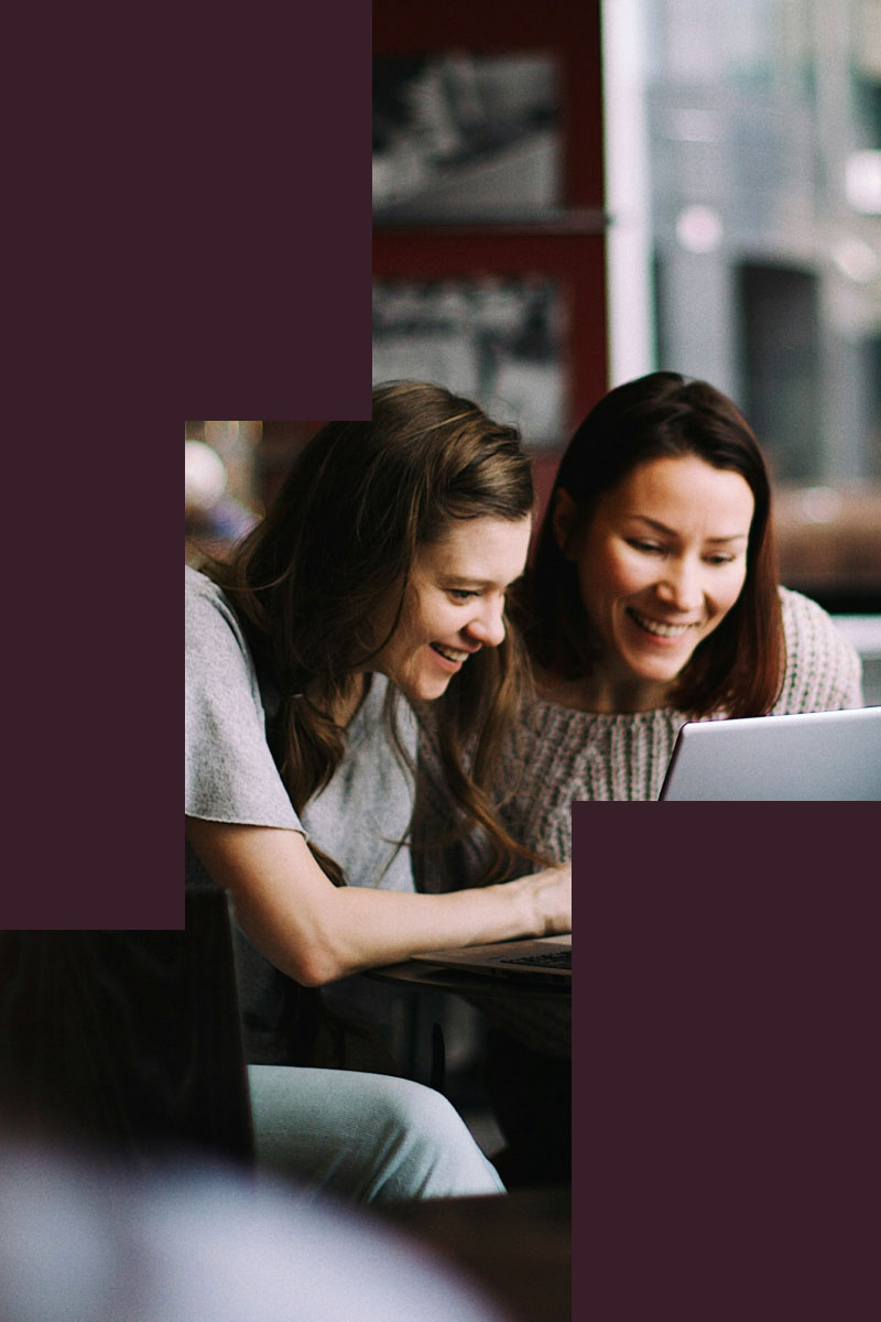 Two women seated at a table, engaged with a laptop, collaborating on a project or discussion.