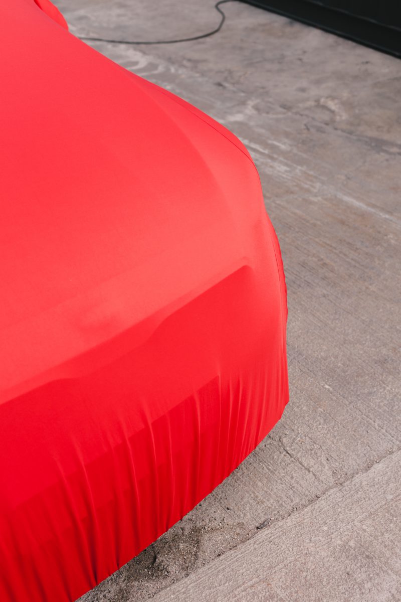 An image of the KIA car covered by a red car cover.