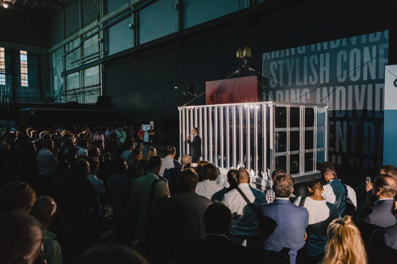 An photograph of someone having a speech in front of the new KIA car, covered by a container.
