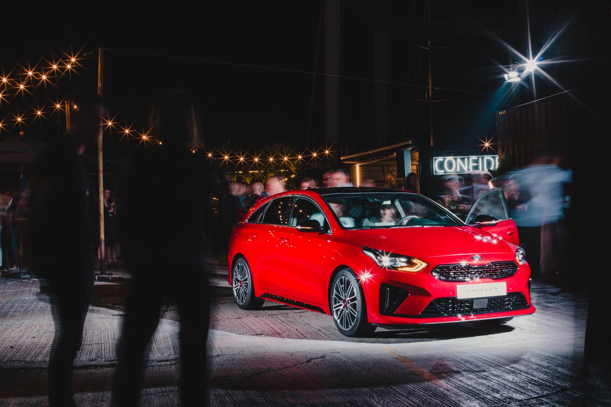 An image of the new KIA proceed car in red, surrounded by people.