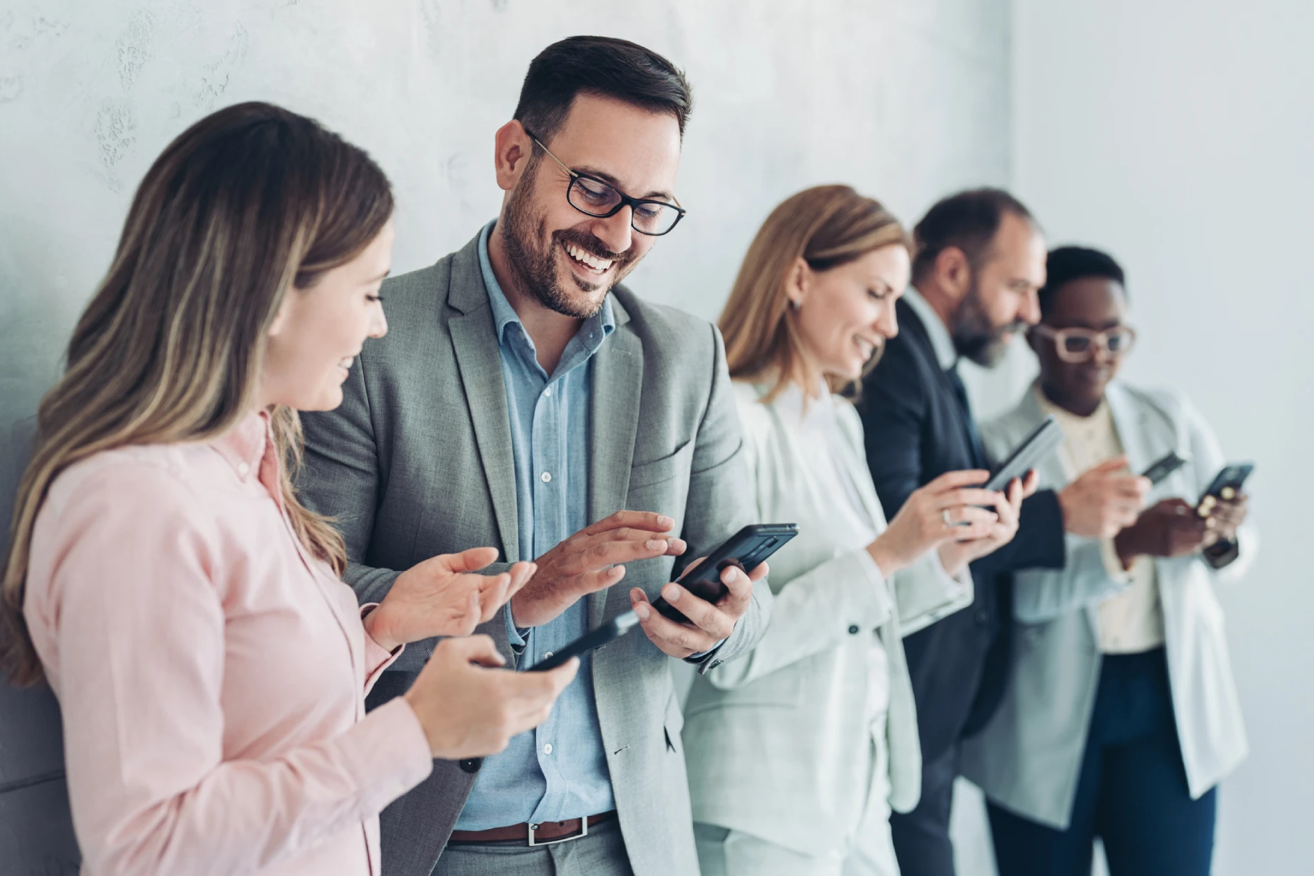 En gruppe forretningsfolk står på rekke og smiler mens de bruker mobiltelefoner, som illustrasjon på moderne teknologi og samarbeid i arbeidslivet.