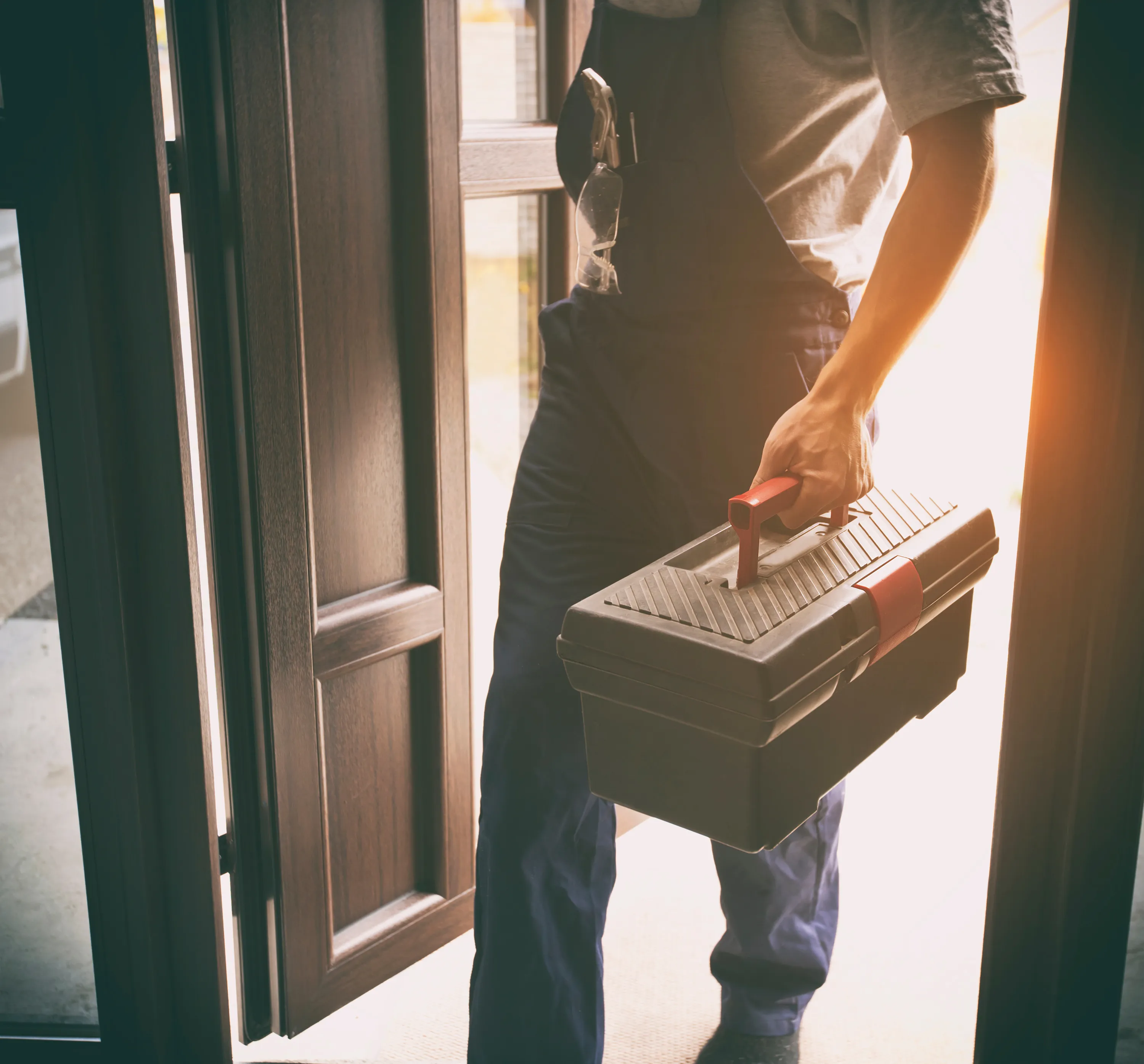 photo of a plumber holding a toolbox with the sun filtering through 2 

