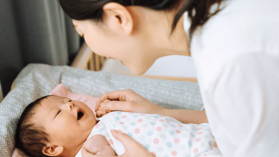 A woman stands beside a crib, holding a baby, embodying warmth and nurturing in a serene setting