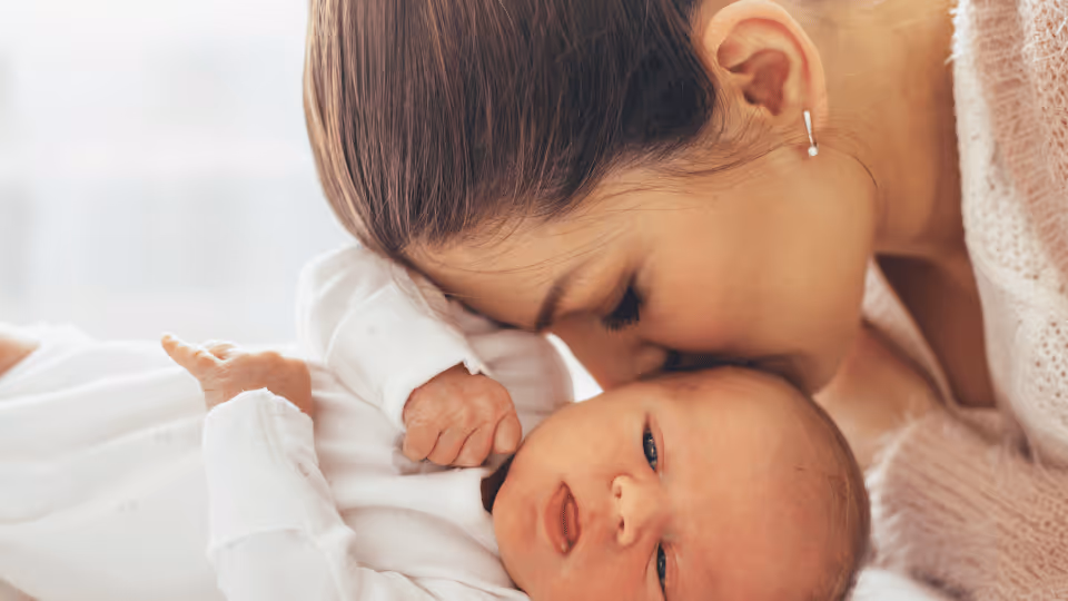 A woman lovingly kisses her newborn baby on the forehead, showcasing a tender moment of affection between mother and child.