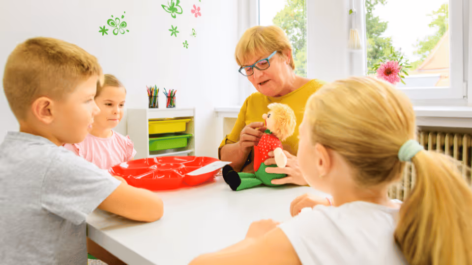 A speech therapist and children gathered around a table, engaging with a doll, showcasing a moment of joy and togetherness