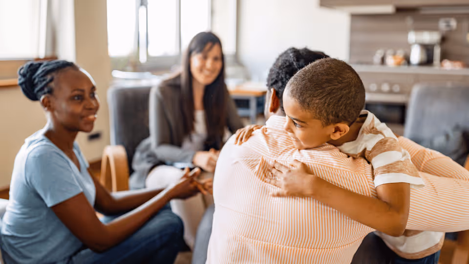 A family sits together at a table, showcasing a child embracing his mother, emphasizing the role of speech therapy in bonding.